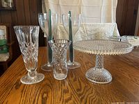 View showing five items including two crystal vases, two tall crystal candlesticks, and hobnail pattern footed cake stand on wood table.