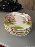 Stack of 12 square-shaped dinner plates with scalloped edges and pink blossom tree design.