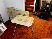 Four vintage TV trays with beige tops featuring painted wheat design and chrome legs, one table opened in front and three folded behind it against a wall.