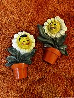 Two vintage plaster flower face wall hangings on orange carpet background, viewed from above.
