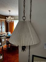Side view showing pleated cream fabric shade and the brass chain hanging from ceiling hook.