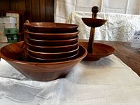 Large walnut salad bowl with six smaller walnut bowls stacked inside, wooden tongs lying alongside, and a 2-tier walnut snack server visible in background