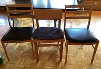 Front view of three wood chairs: two with black seats, one with blue seat cushion