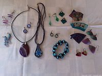 Assorted art glass earrings, two pendant necklaces, beaded bracelet, and several pins arranged on white cloth