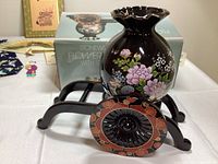 Black stoneware flower vase with floral designs on a black rickshaw stand with red and gold decorative details, photo showing vase and stand with packaging box in the background.