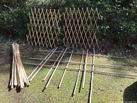 Wide view of bamboo poles, collapsible lattice panels, and woven trellis on grass outdoors.
