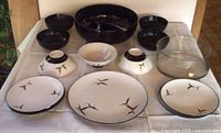 Set of black and white plates and bowls with Asian bamboo design, including bowls upside down and one large clear glass bowl