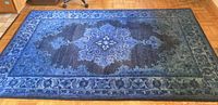 Full view of rectangular blue wool rug on wooden floor, showing central medallion design and border pattern.