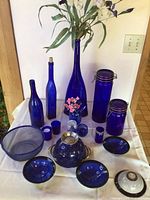 Full view of lot showing cobalt glass bottles, vase, canisters, bowls, votives, colander and strainer arranged on table.
