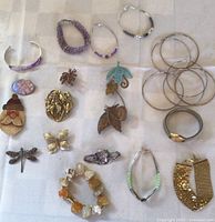 Photo of assorted costume jewelry pieces including multiple bracelets, pins, and silver-tone bangles arranged on a cloth.