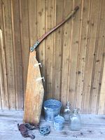 Full lot showing wooden rudder leaning against wooden wall with metal pails and glass jugs on the floor.
