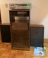 Overall lot showing Fisher audio receiver atop a Sony audio cabinet with glass front, two speakers placed on floor alongside, and some manuals on floor.