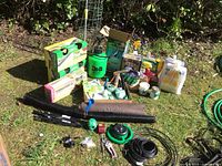 Wide view of all items including landscaping edging, sprayers, boxed amendments, irrigation tools, gloves, and seed packets arranged on grass.