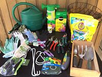 Photo showing green watering can, multiple gloves, hand tools in wooden box, and gardening accessories