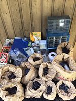 Overview of hardware lot including paper bags filled with nails, plastic storage organizers, rolls of white string, and packaged nails/staples.