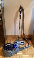 Full view of LG Kompressor canister vacuum with hose connected, showing dark gray and blue body, wand, and vacuum head in use position.
