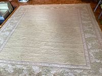 Full view of the large pale yellow wool area rug showing the subtle rectangular central field and surrounding leaf-pattern border.