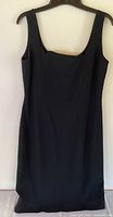 Front view of little black dress on hanger showing sleeveless design and square neckline