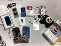 Overview of all lot items laid out on table including iPods, Message Mates, speakers, cables, earphones, and accessories