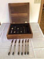 Wooden box open showing some flatware pieces laid inside with knives laid outside the box on tablecloth