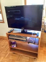 Samsung 32-inch LCD TV on wooden rolling stand showing screen with no signal message, remote on top shelf, Toshiba DVD/VHS player below