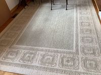 Full view of the rug laid out on a hardwood floor showing central field and border pattern