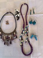 Full view of two necklaces with beads and parrot pendants, parrot pin, and multiple pairs of earrings in different colors and styles on white background.