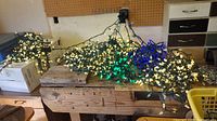 Multiple LED light strands with white and blue bulbs, tangled and laid out on a wooden workbench. Includes green wiring.