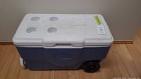 Blue and white Coleman cooler with lid closed, showing top cup holders and label on lid.