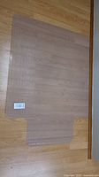 Clear transparent plastic floor protector mat on wood floor, showing full shape and size.