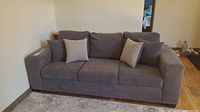 Front view of grey 3 seater couch with four pillows (two solid grey, two checkered).
