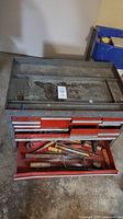 Front and open view of red metal tool chest showing open drawers with tools such as chisels and screwdrivers inside.