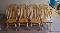 Group of eight solid oak dining chairs lined up in two rows with visible natural wood finish and spindle backs.