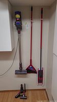 Dyson V8 vacuum hanging on wall mount next to Vileda broom and dry mop