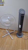 Both fans standing on the floor side by side, showing the pedestal fan and tower fan.