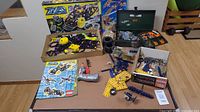 Wide view of all parts and kits laid out including Lego ZNAP boxes, instruction manuals, metal toolbox and loose components spread on flat surface