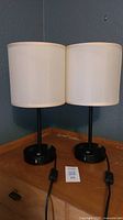 Two black touch lamps with cream shades placed side by side on a wooden surface, showing overall design and size.