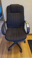 Front view of black fabric office chair showing padded seat and backrest, armrests, and caster base.