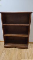 Front view of the dark solid wood 3 shelf bookcase, showing overall structure and condition.