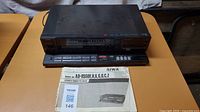 Front view of the AIWA AD-R550 stereo cassette deck with manual and original box on table.