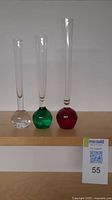 Three tapered bubble glass single stem vases in clear, green, and red placed side by side on a wooden surface