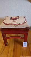 Front view of the footstool with a decorative rooster pillow on top showing design details