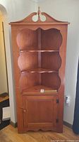 Full view of vintage Vilas corner cabinet showing three shelves and closed cupboard door below.