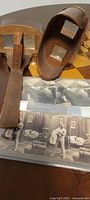 Photo showing two antique wooden stereoscopes and two stereoscopic cards placed on a table; stereoscopes have wooden handles and lenses visible, cards show black and white images.