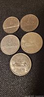 Five Canadian silver dollar coins on dark textured surface showing both obverse and reverse.