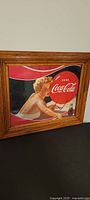 Framed vintage Coca-Cola print showing a blonde woman holding a glass of Coke, in wooden frame with glass, approx 18 x 15 inches