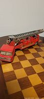 Side view of vintage tin litho fire truck with extended metal ladder trailer on checkered table surface.