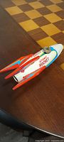 Side view of the tin toy rocket showing the painted Atomic Rocket label, red fins with blue lightning bolt design and the key wind on top.