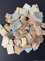 Photo of a large assortment of paper packets and envelopes containing various mainsprings for vintage watches, laid out on black background.