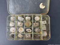 Top-down photo showing a plastic divided box containing 19 vintage watch dials and movements, mostly Bulova